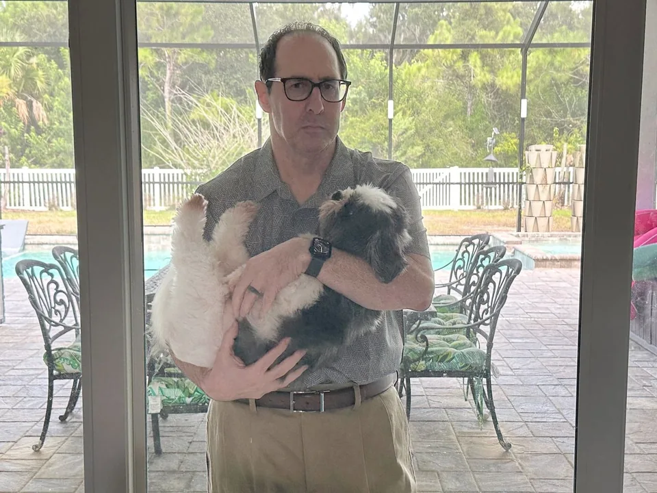 Author Phil Weiss looking out through a window while holding one of his dogs